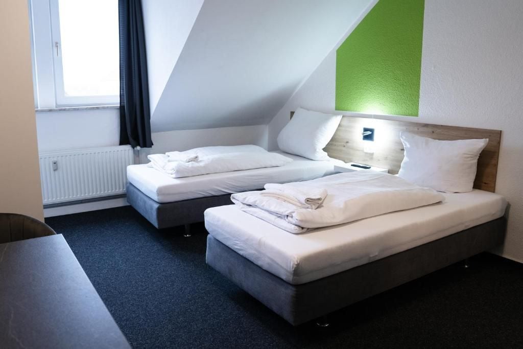 Habitació d'hotel amb dos llits, una taula i una finestra amb cortines.