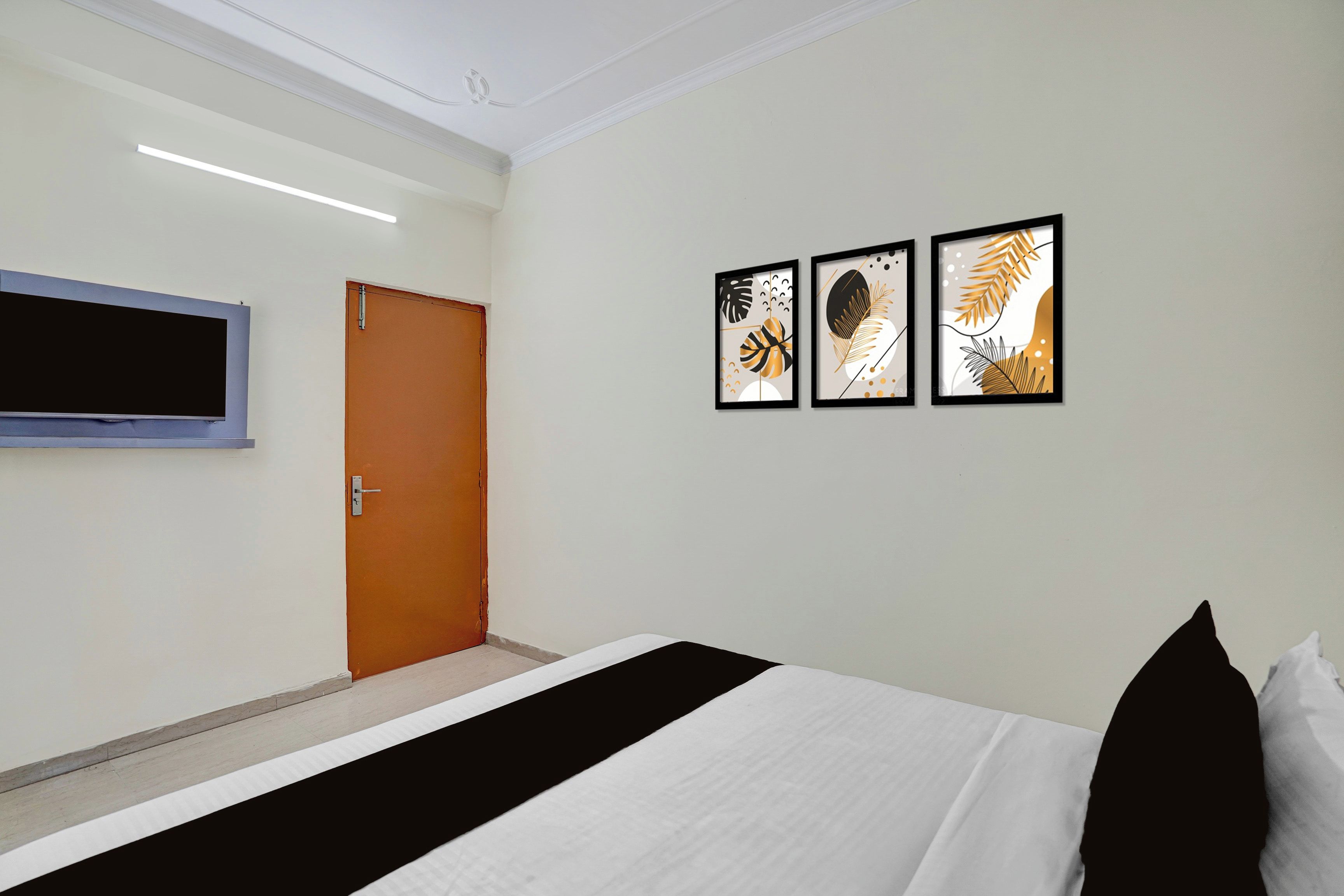 Une chambre d’hôtel comprenant un lit, une porte, un téléviseur à écran plat fixé au mur et trois œuvres d’art encadrées.