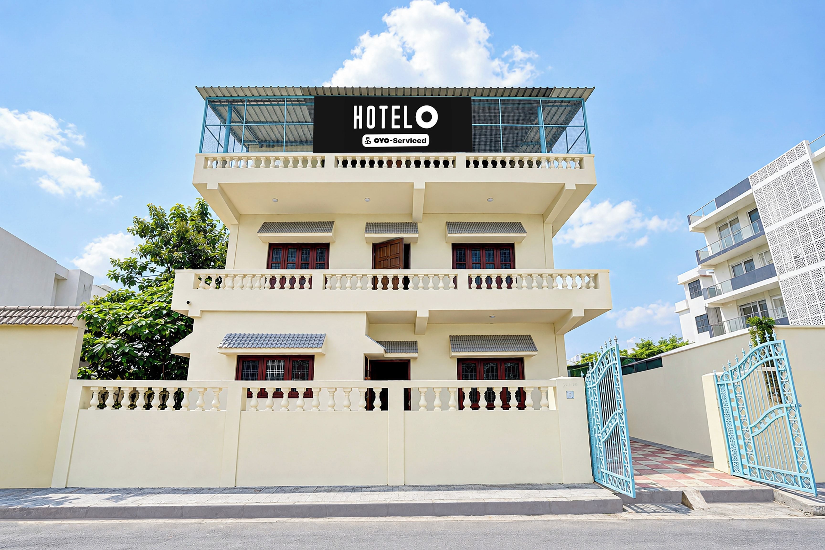 Un hôtel à plusieurs étages, reconnaissable à son enseigne bien visible au sommet, à son entrée sécurisée par un portail et à son balcon situé à l’étage supérieur.