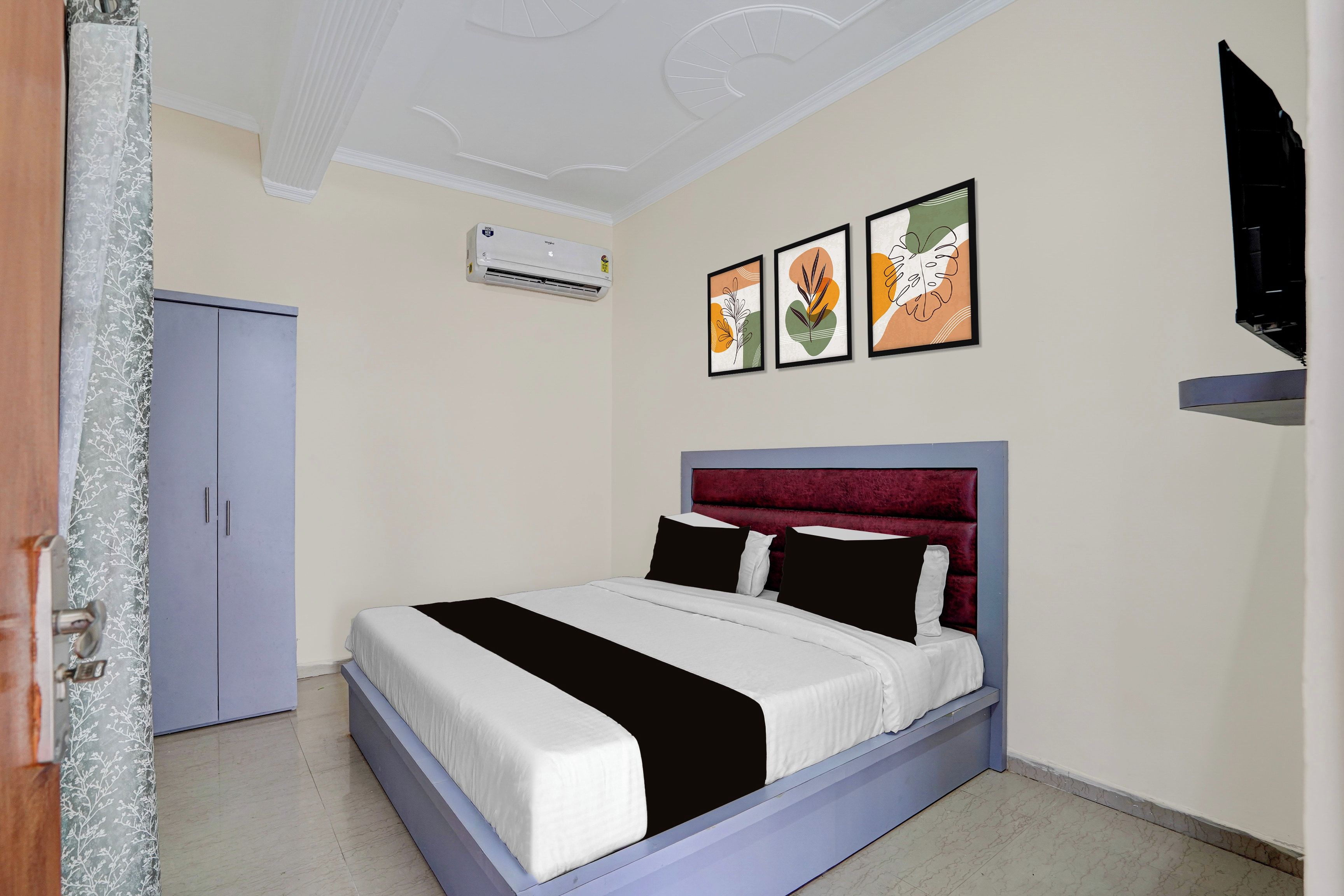 A bedroom with a bed, a wardrobe, a flat-screen TV, and an air conditioning unit.