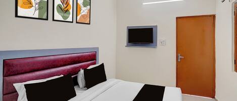 Una habitación de hotel con una cama, un televisor montado en la pared y tres obras de arte enmarcadas sobre la cama.