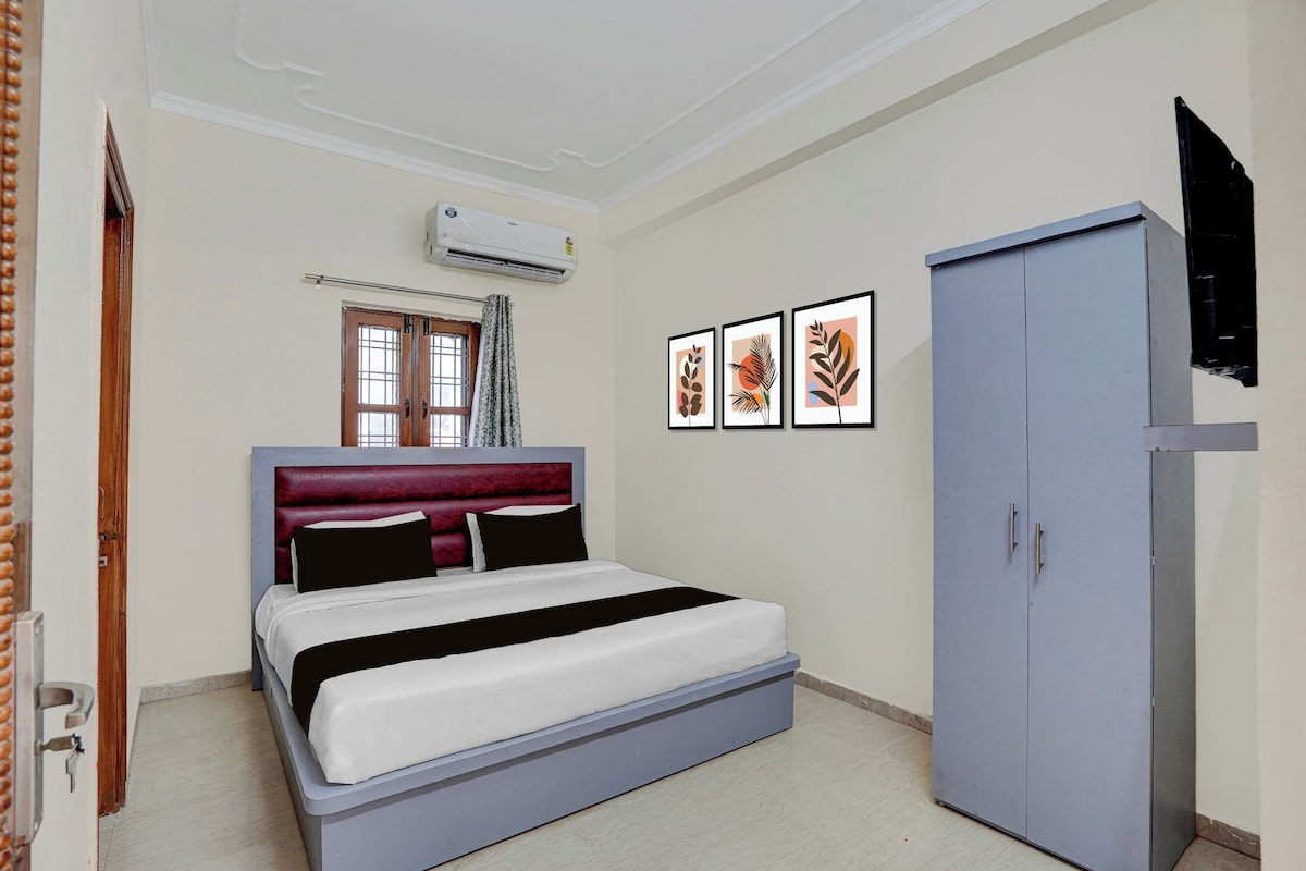 Un dormitorio con cama, armario, aire acondicionado, ventana y tres cuadros en la pared.