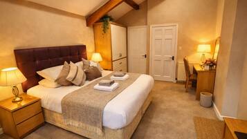 A hotel room with a large bed, bedside lamps, a wooden nightstand, a desk with a chair, and a door.