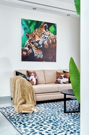 Een woonkamer met een bank, een bijzettafeltje, een kamerkleed met een patroon en een groot schilderij van een luipaard.