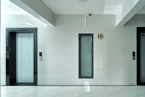Een moderne lift met glazen deur, een digitaal scherm dat verdieping 17F weergeeft, en een bedieningsknop aan de muur.