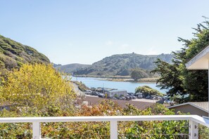 A coastal view with a parking area, a building with a flat roof, and a hill with dense vegetation. - 2BR Coastal Retreat w/ River & Sea Views (Jenner)