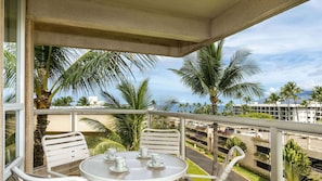 A balcony with a table and chairs, overlooking a parking area and palm trees. - Maui Banyan- Hotel Room Resort View- Beach across the street/Free Parking (Kihei)
