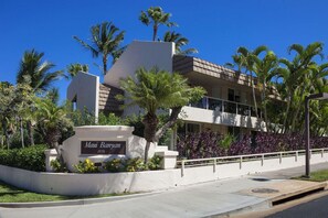 Um hotel moderno com fachada branca, palmeiras e uma placa indicando "Maui Resort 2575".
