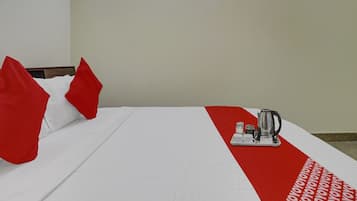 Een hotelkamer met een bed, kussens en een dienblad met een waterkoker en kopjes.