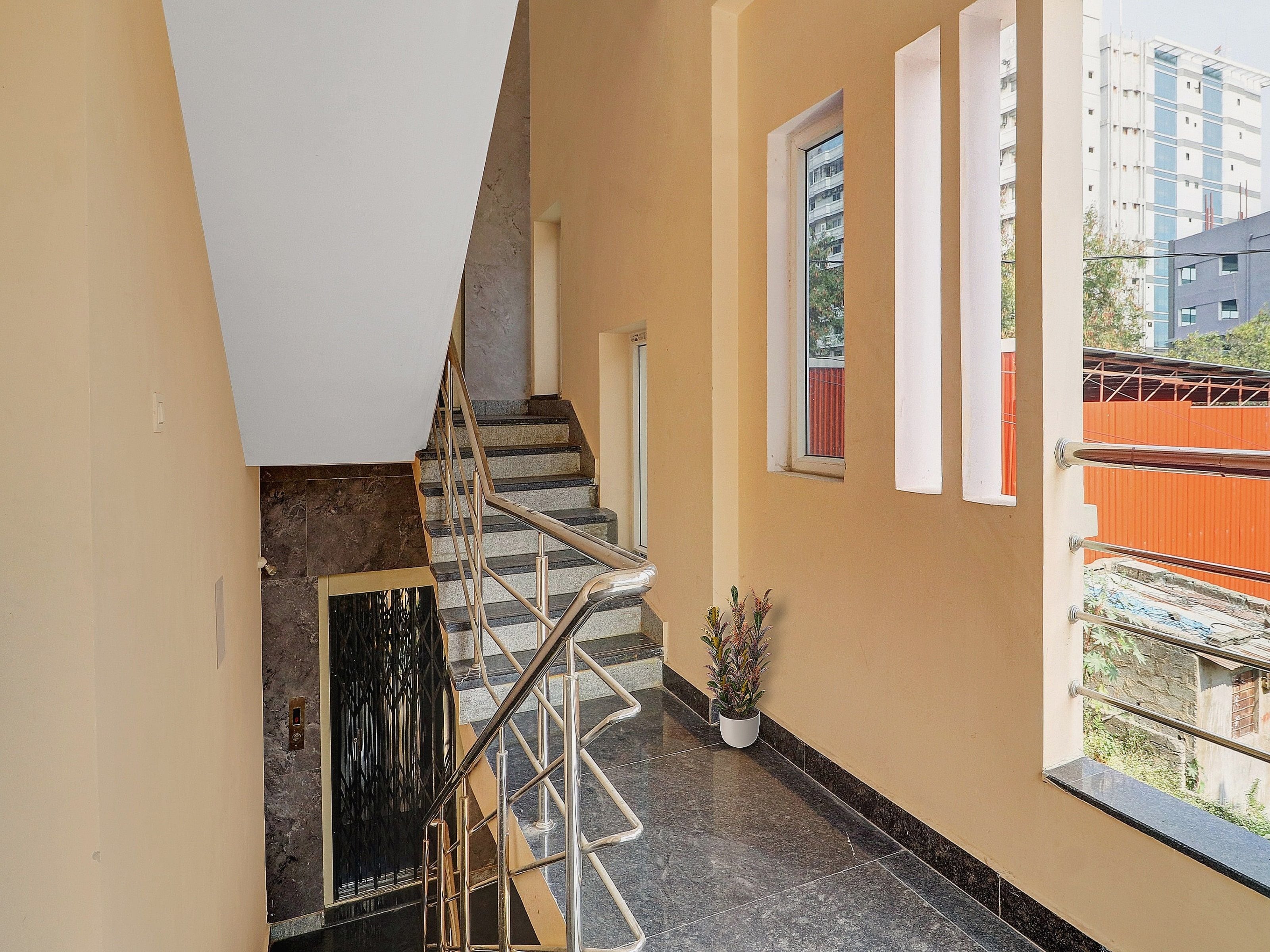 A staircase with a handrail, a potted plant, and a window with a view of buildings.