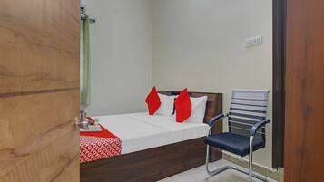 A hotel room with a bed, a chair, a table with a red and white patterned tablecloth, and a wall-mounted air conditioning unit.