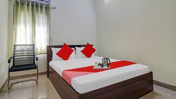 Habitación de hotel con cama, una silla, mesita de noche con hervidor y equipo de aire acondicionado.