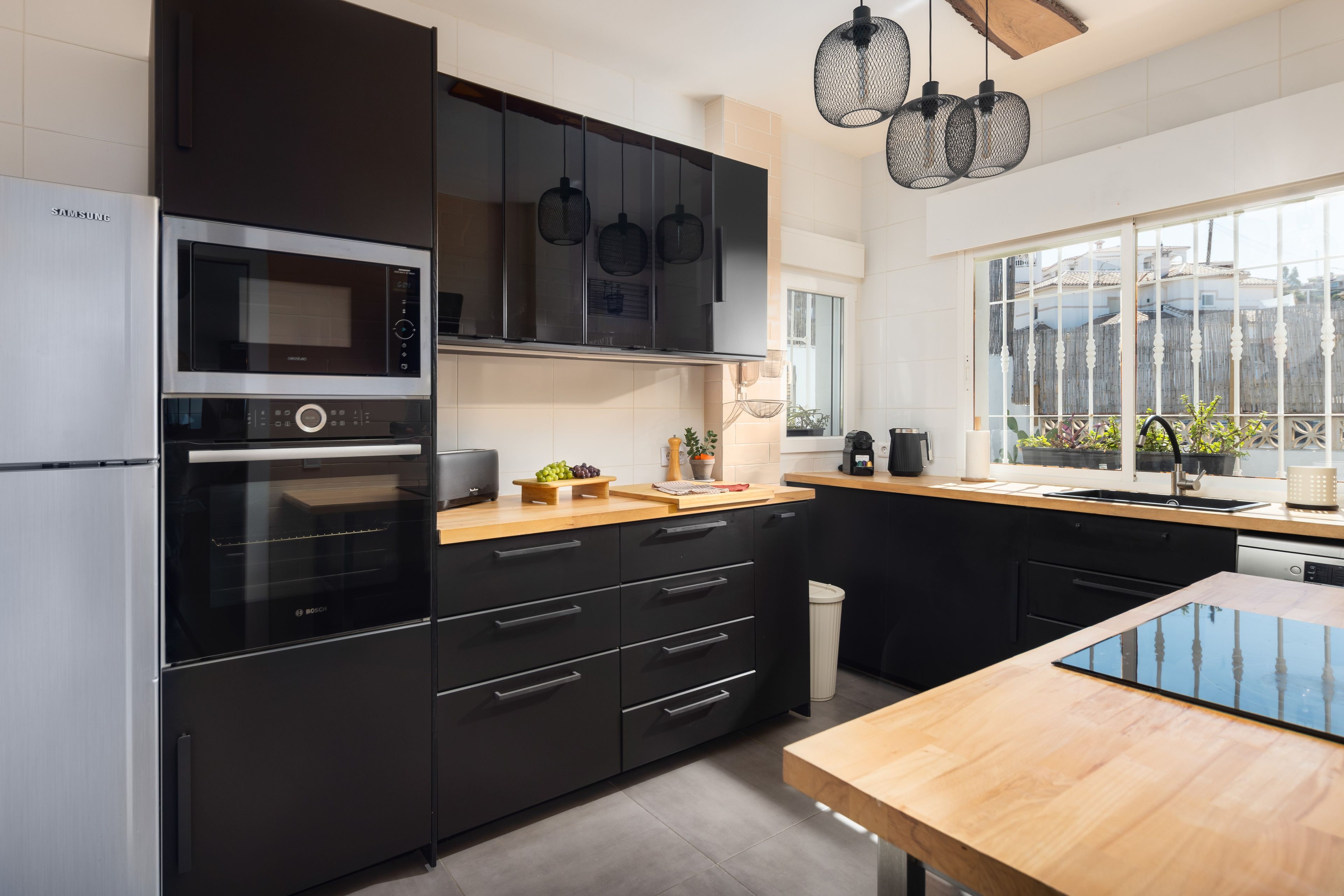 Una cocina moderna con armarios negros, electrodomésticos de acero inoxidable y encimera de madera.
