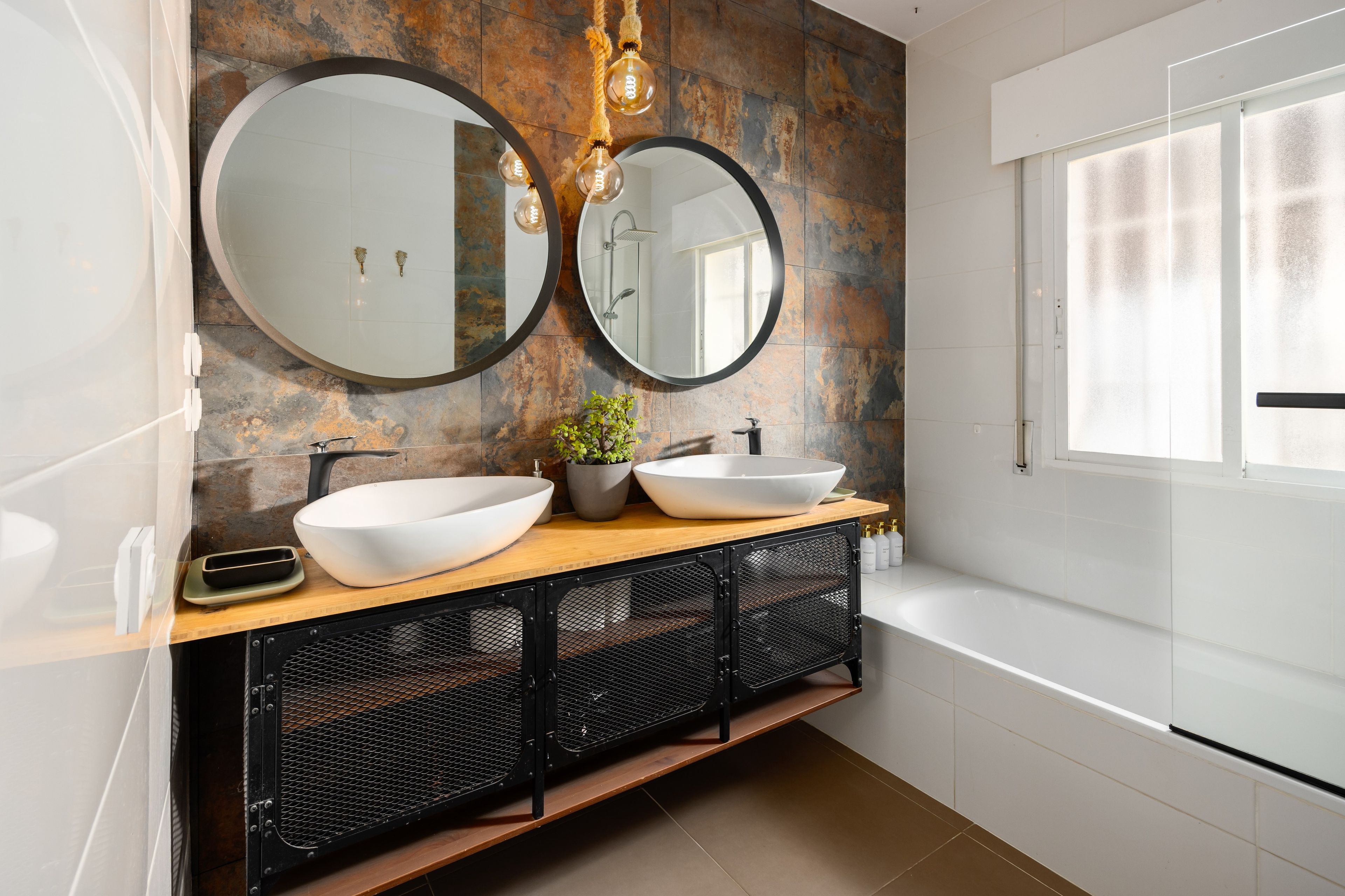 Een moderne badkamer met twee ronde spiegels, een wastafel en een bad.
