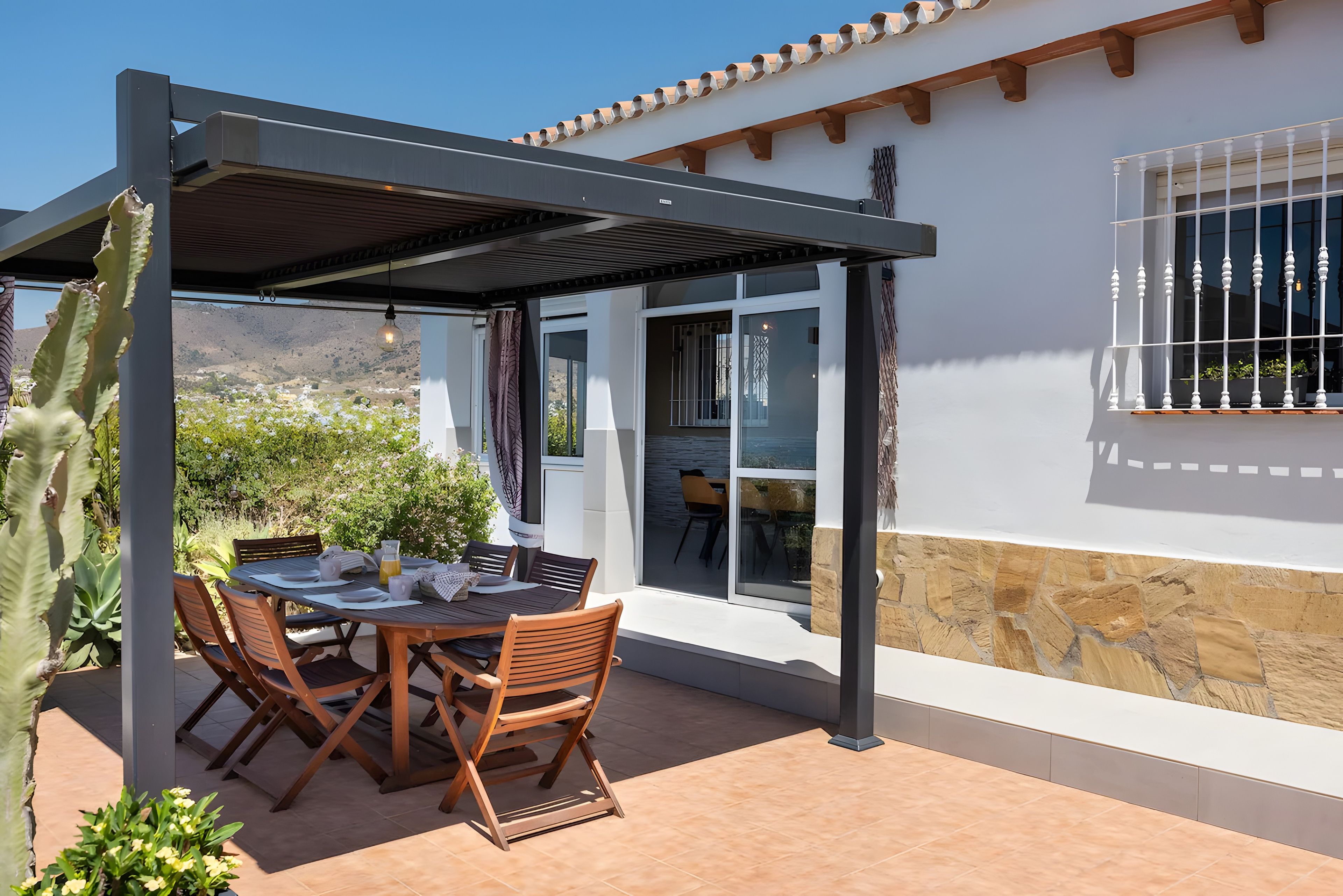 An outdoor patio with a table and chairs, a pergola, and a view of a mountainous landscape.