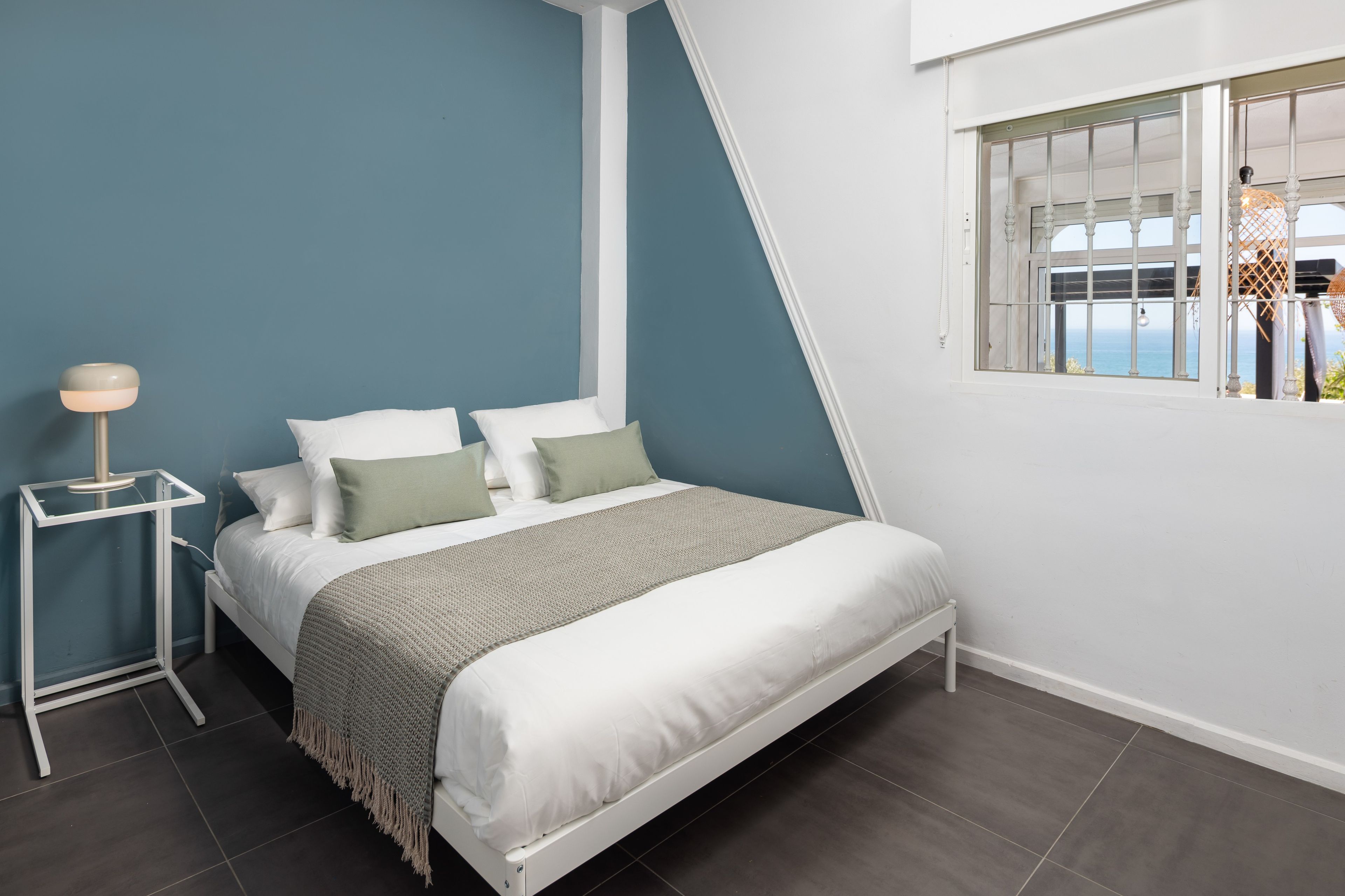 Un dormitorio moderno con cama, mesita de noche y ventana con vistas.