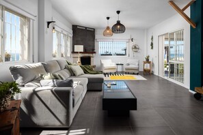Un salon moderne avec un canapé d’angle, une cheminée et de grandes fenêtres.