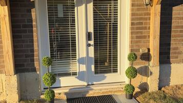 A wooden-framed entrance with a metal door, a small step leading up to the door, and two potted plants on either side.