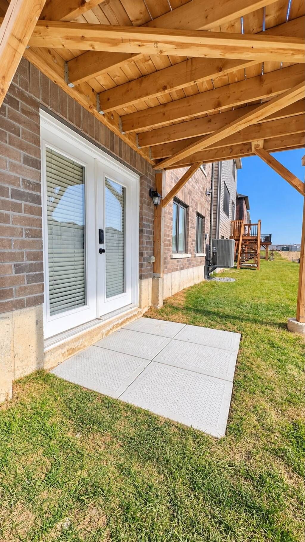A covered patio area with a brick wall, a sliding glass door, and a concrete walkway leading to a grassy yard.