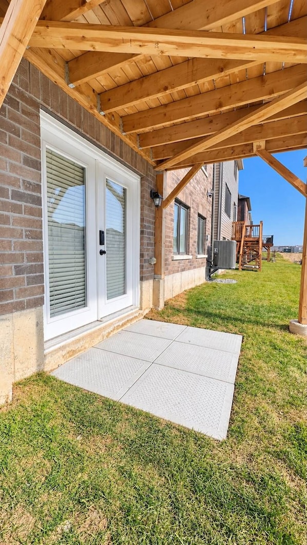 A covered patio area with a brick wall, a sliding glass door, and a concrete walkway leading to a grassy yard.