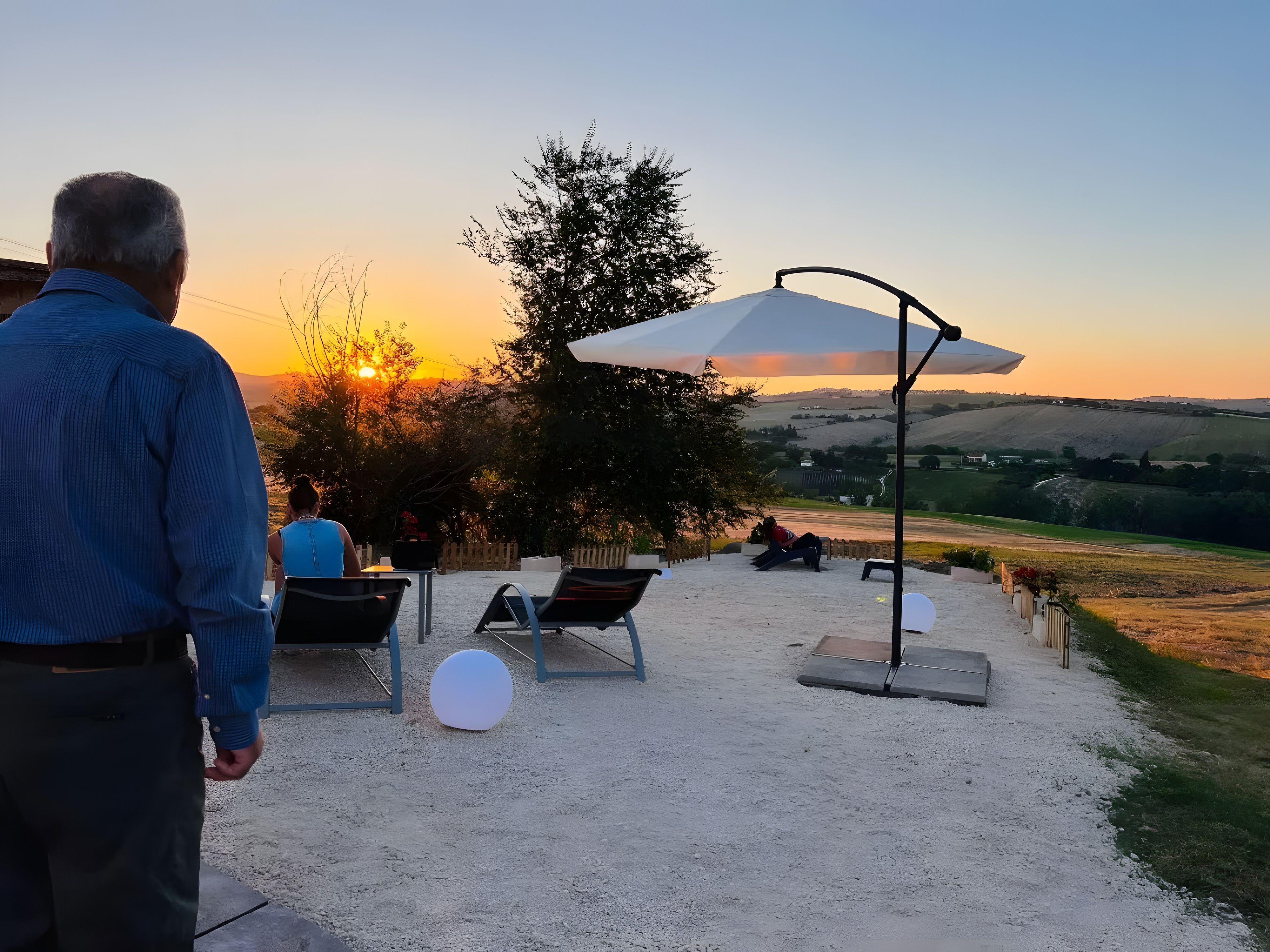 An outdoor seating area with a view of the sunset, a large umbrella, and a gravel path.