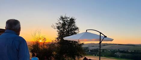 An outdoor seating area with a view of the sunset, a large umbrella, and a gravel path.