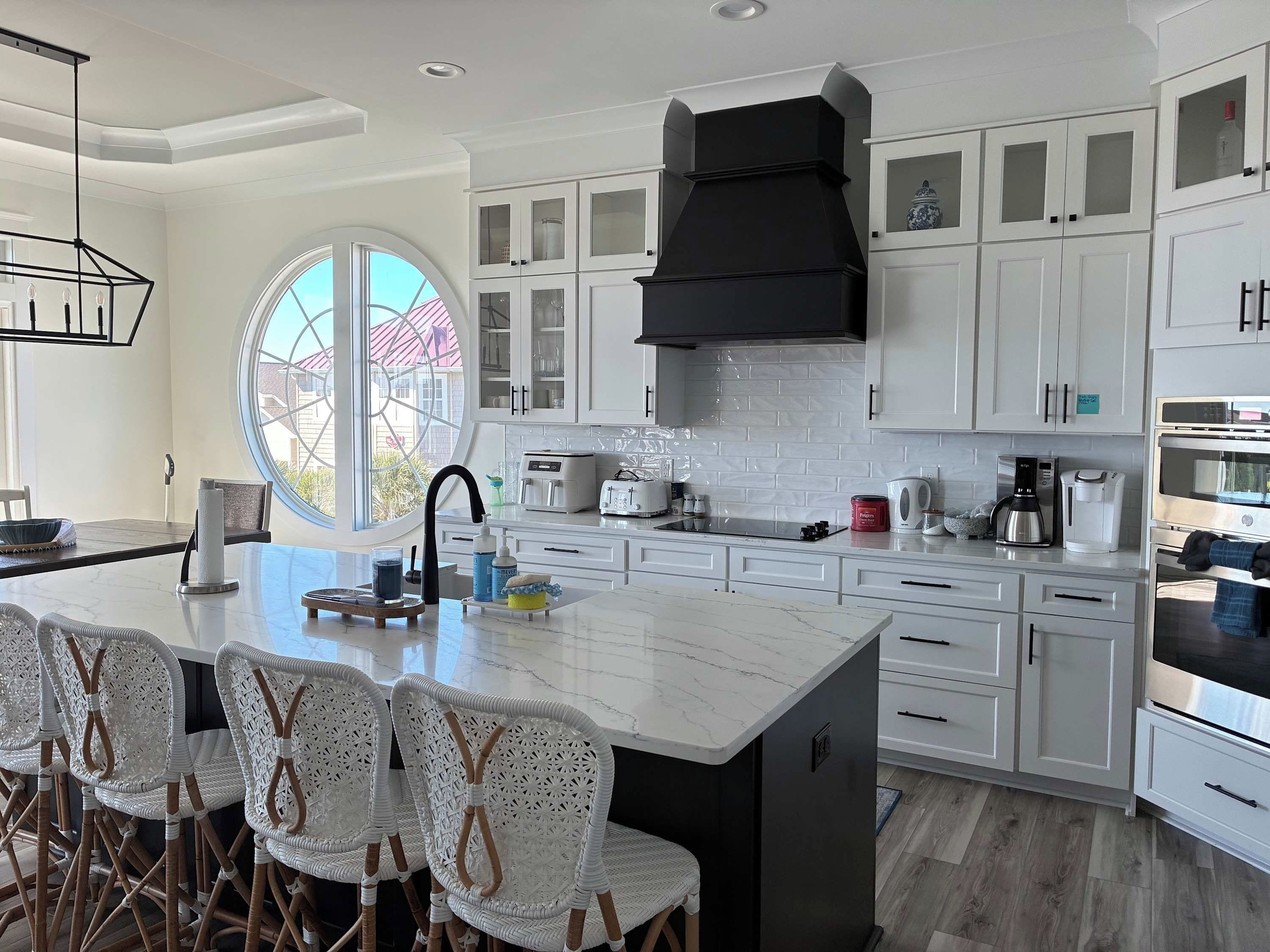 A modern kitchen with white cabinetry, a black hood, and a large island with seating.