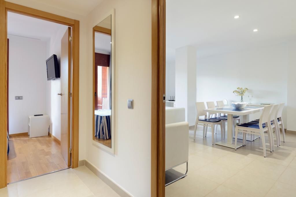 Un espace repas moderne avec une table et des chaises blanches, une petite table d’appoint et une plante en pot.
