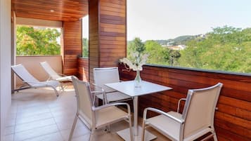 Ein Balkon mit Holzboden, weißen Stühlen, einem Tisch und einer Blumenvase.