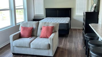 Una habitación con techo de madera, una cama con cabecera oscura, un sofá gris con cojines rojos, un mueble negro y una encimera de mármol.