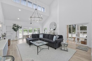 A spacious living room with a large sectional sofa, a glass coffee table, and a ceiling light fixture. - Bridge-Way Villas at Pelican Bay (Naples)