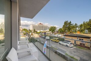 Un balcón con mobiliario de mimbre, vista a un estacionamiento y edificios al fondo.