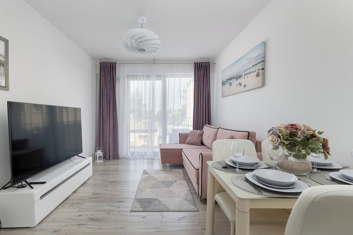 Una sala de estar moderna con un televisor de pantalla plana, un sofá, una mesa de comedor para dos personas y un cuadro en la pared.