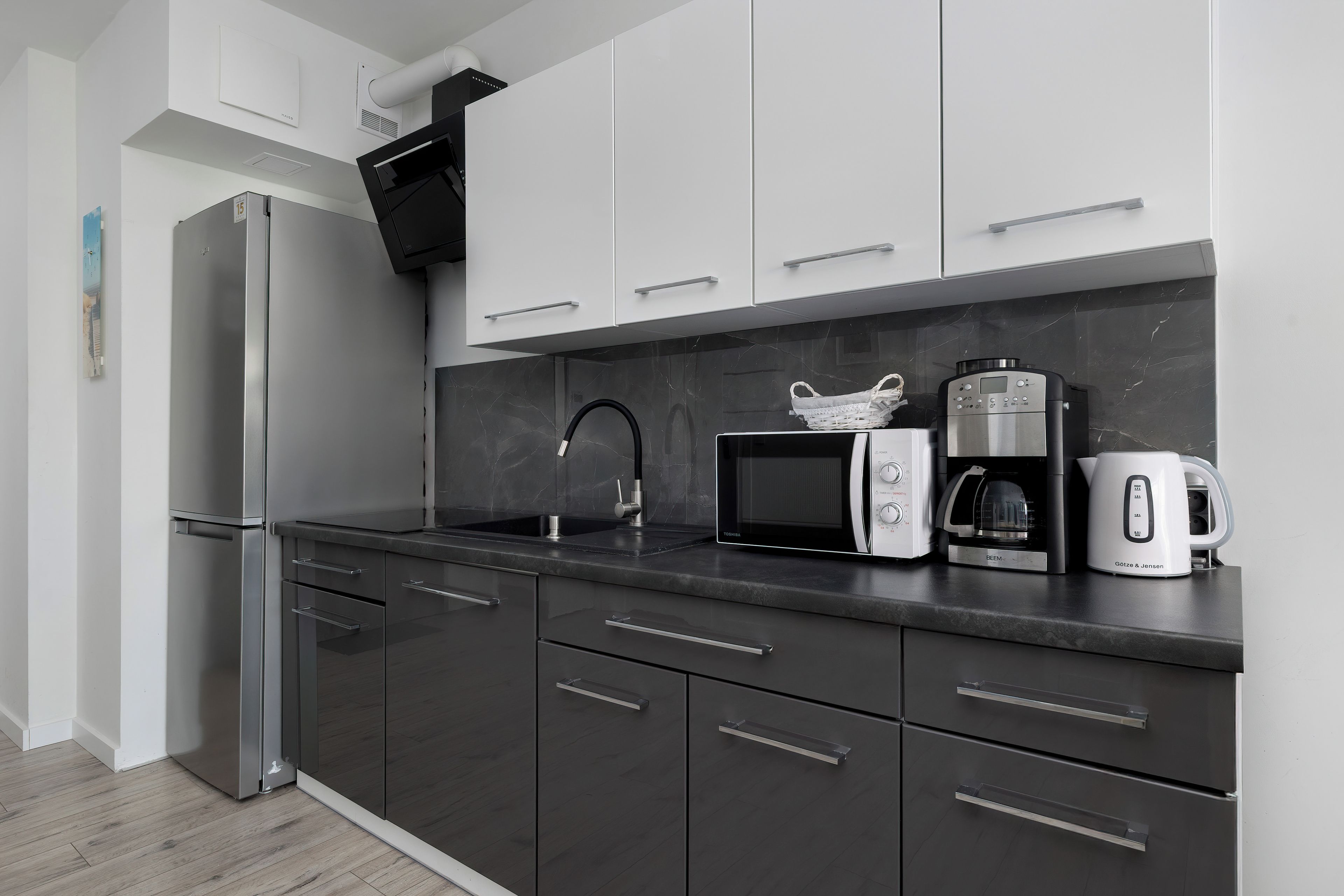 A modern kitchen with a refrigerator, microwave, coffee maker, and kettle.
