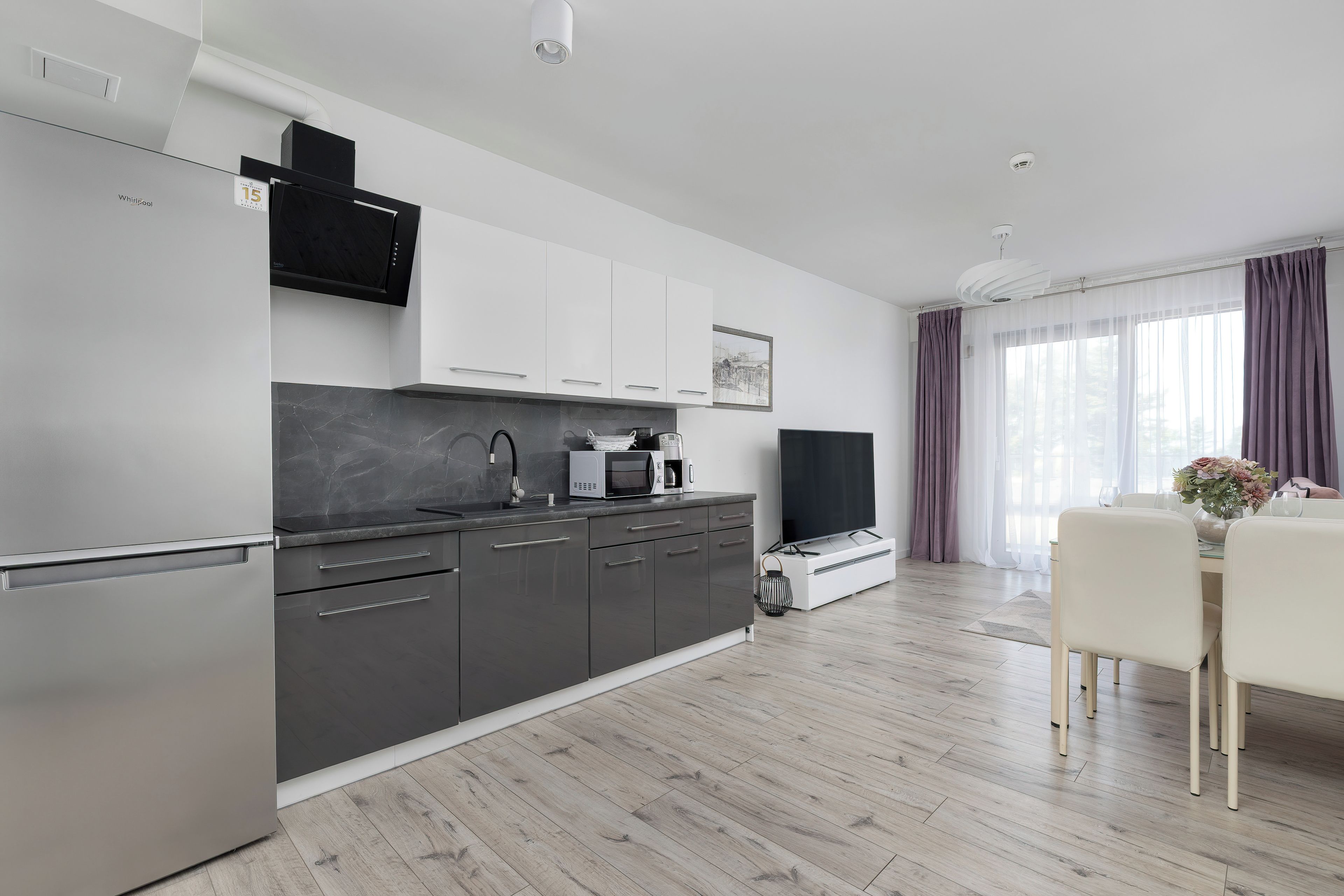 A modern kitchen with a built-in microwave, a large flat-screen TV, and a dining area with a table and chairs.