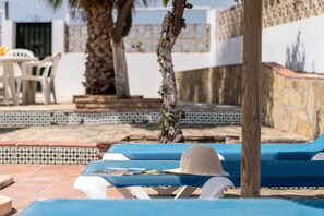 Un espace aménagé au bord de la piscine, avec des chaises longues et une table, une piscine carrelée et un mur en pierre.