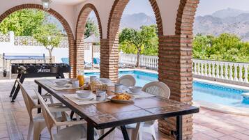 A covered outdoor dining area with a pool, brick arches, and a view of mountains.