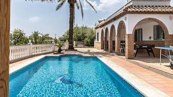 A swimming pool with a clear blue water surface, surrounded by a white fence and a palm tree.