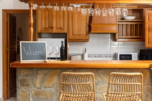 Une cuisine avec des meubles en bois, un plan de travail en pierre, une pancarte de bienvenue, des verres à vin et une bouteille.
