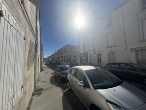 Eine enge Straße gesäumt von parkenden Autos und Gebäuden, die Sonne scheint hell.