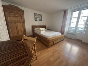 A bedroom with a wooden bed, a nightstand, a wooden wardrobe, and a window with curtains. - Le Gambetta, au centre ville (La Rochelle)