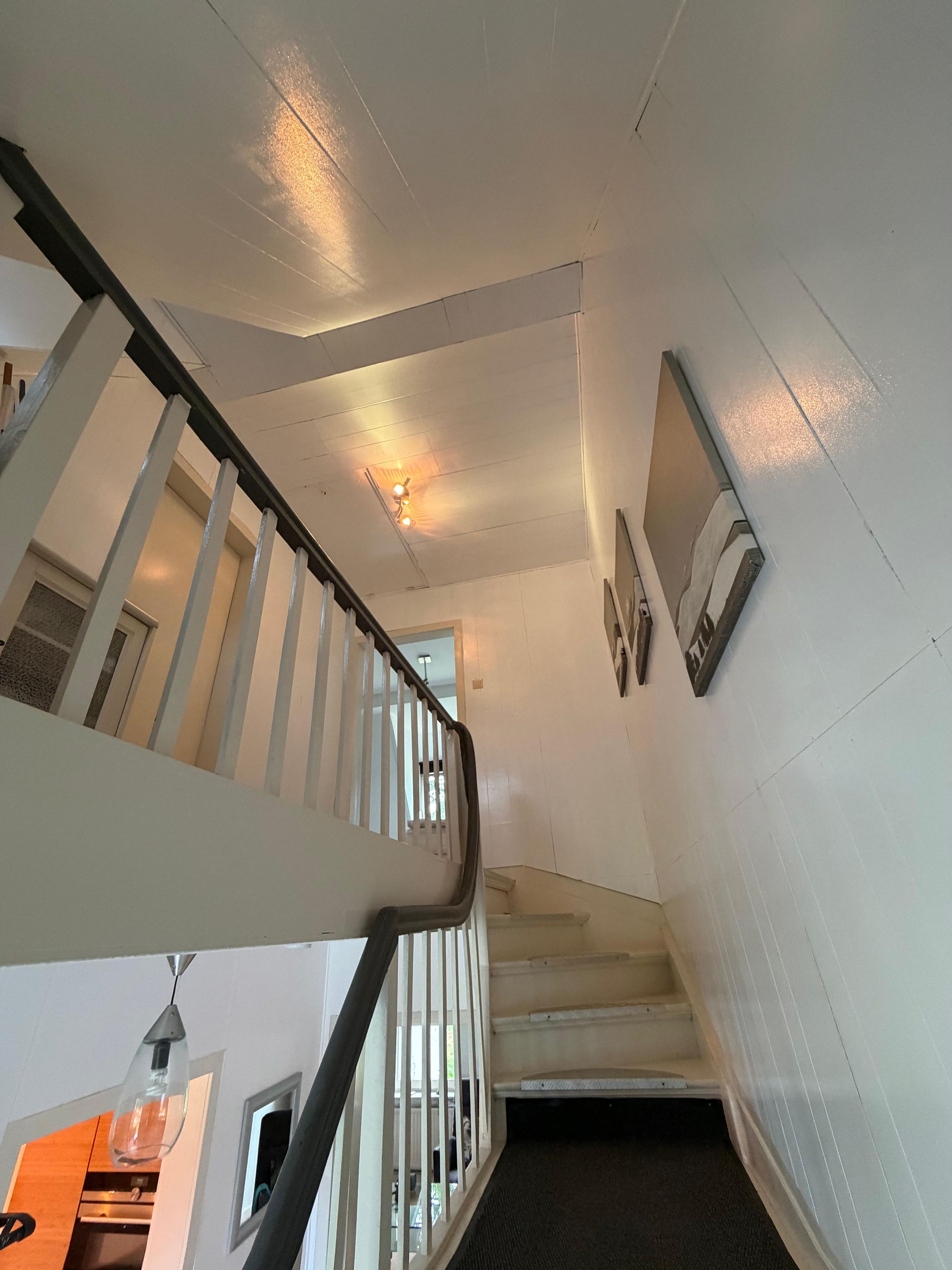 A staircase with white railings and a handrail, leading to a landing with a light fixture and a wall-mounted picture frame.