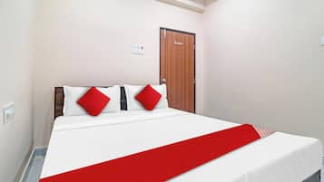 A hotel room with a bed, a wooden door, and a light switch on the wall.