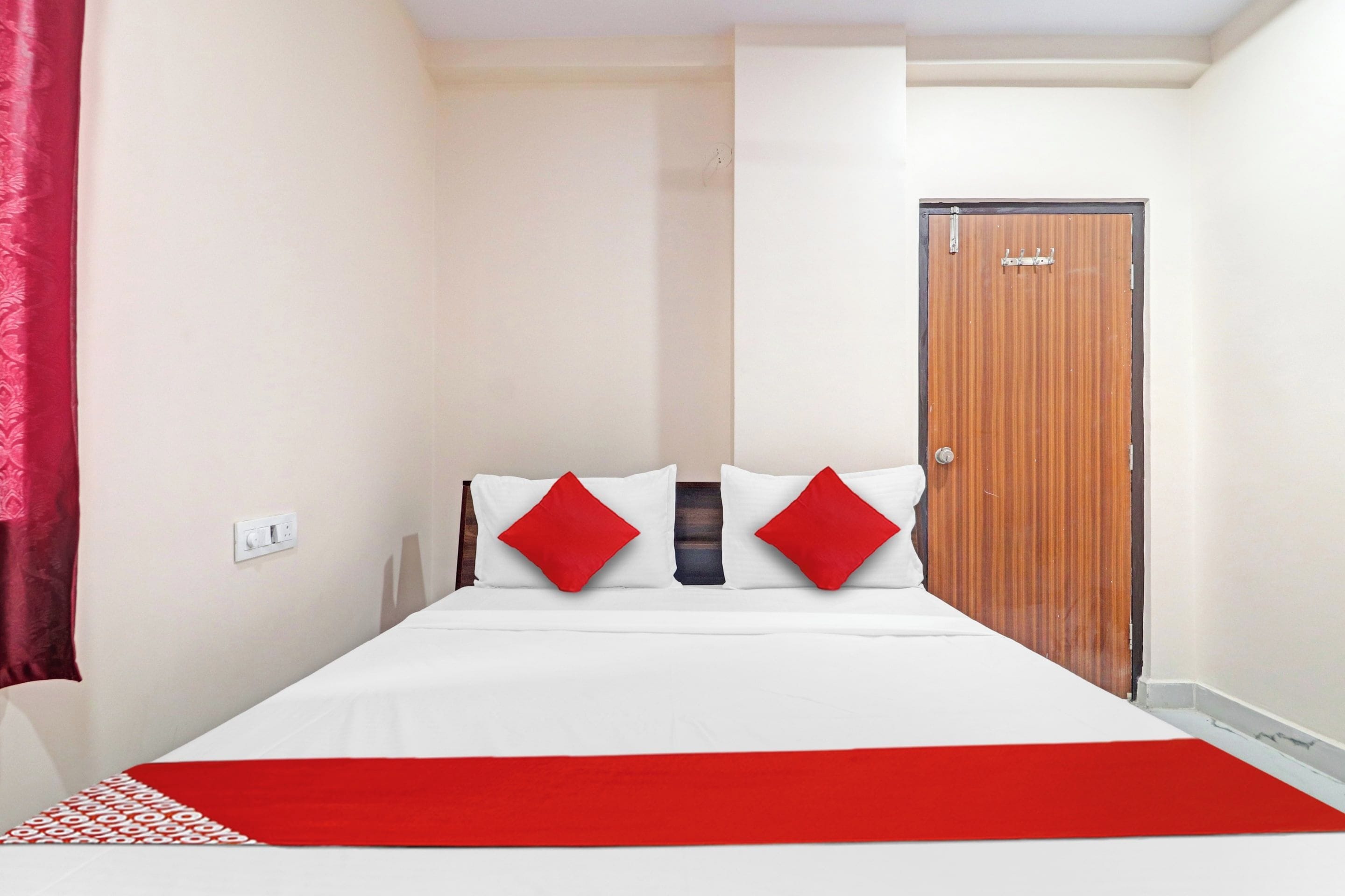Quarto de hotel com uma cama, um cobertor vermelho e uma porta de madeira.