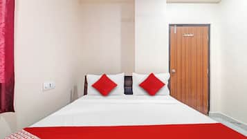 Quarto de hotel com uma cama, um cobertor vermelho e uma porta de madeira.