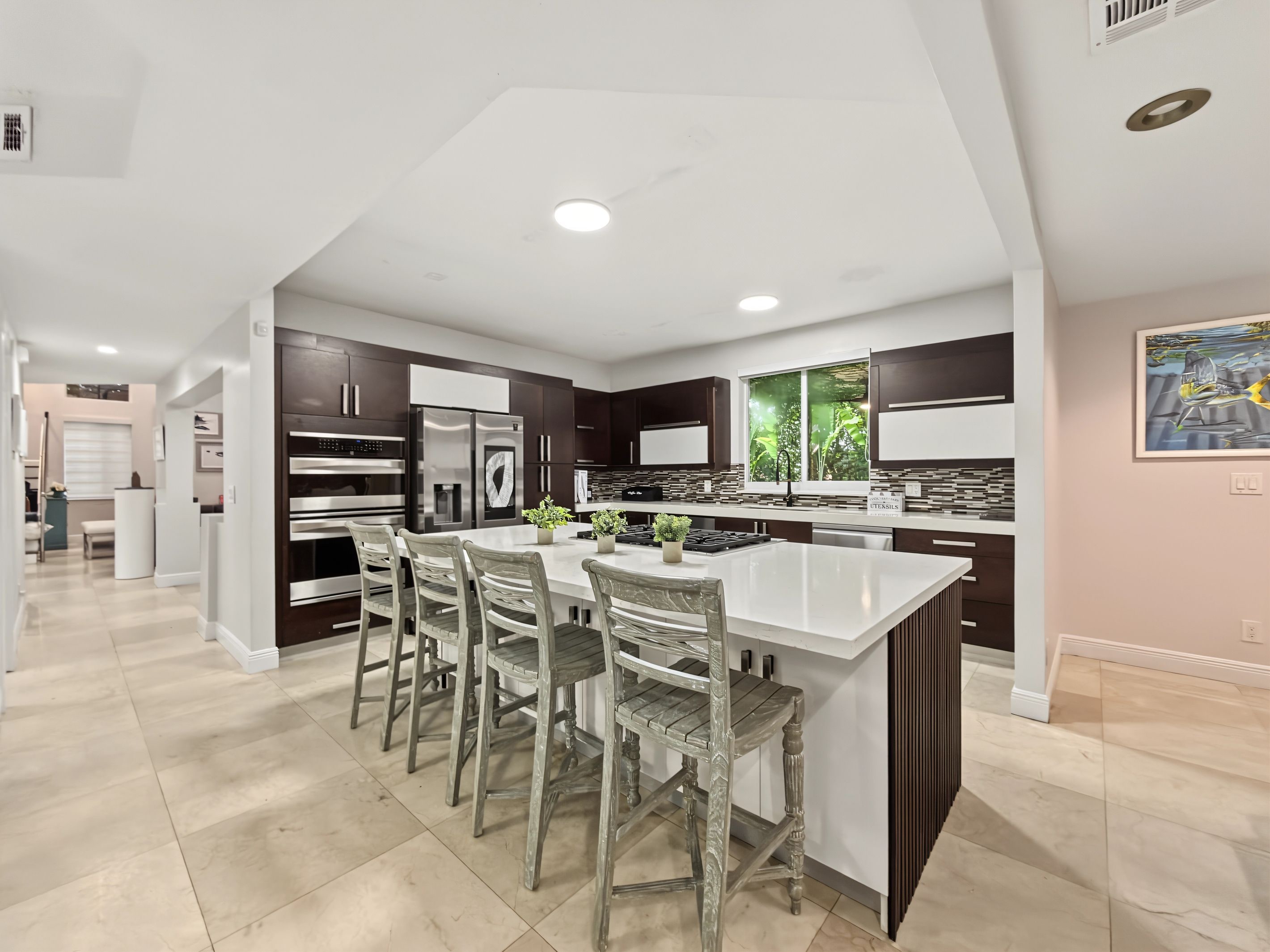A modern kitchen with a central island, dark cabinetry, stainless steel appliances, and a dining area with chairs.