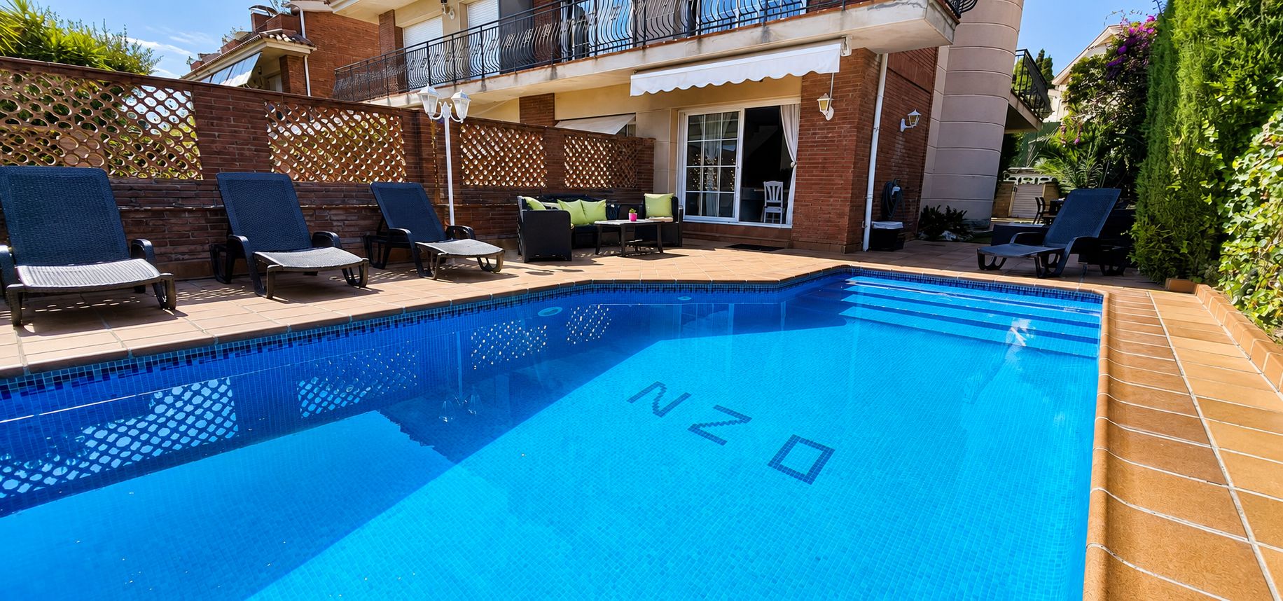 Una piscina con sillones de descanso y un patio.