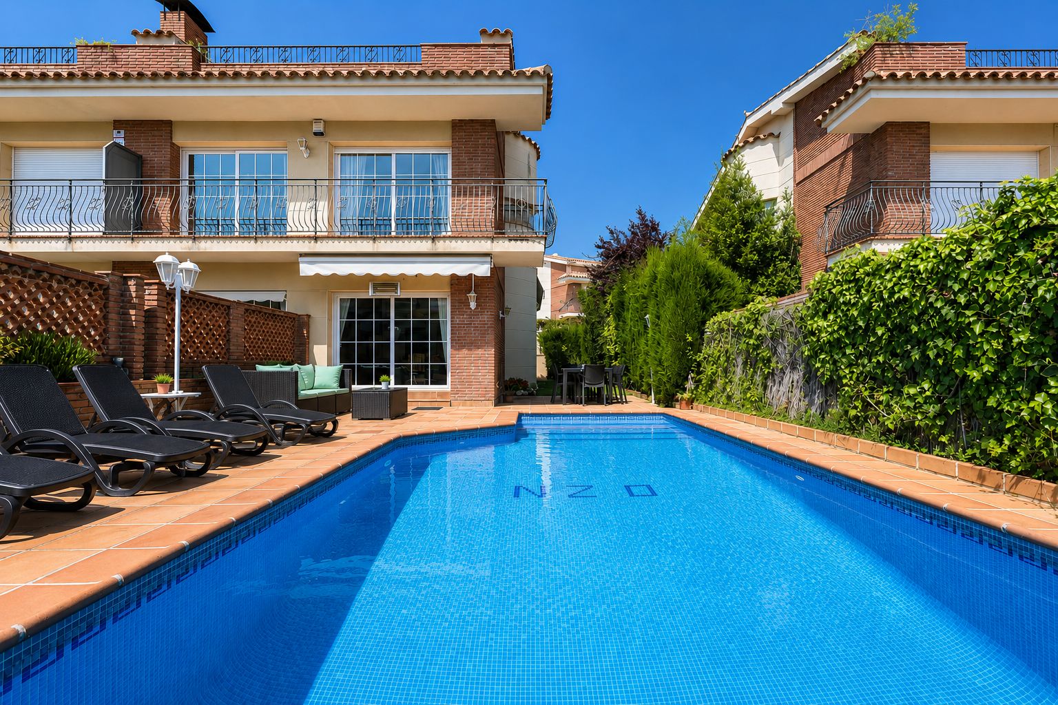 Una casa de dos pisos con piscina, mobiliario exterior y un jardín bien cuidado.