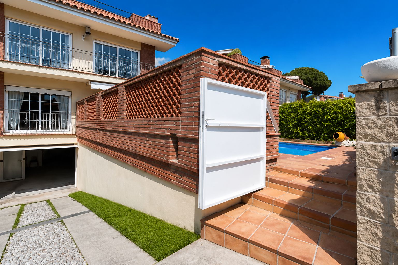 Una propiedad residencial con fachada de ladrillo, puerta blanca, piscina y muro de piedra.
