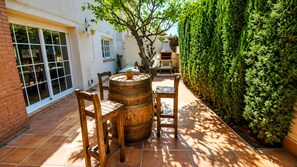 Un patio con una mesa y sillas de madera redonda, un barril y un muro de ladrillo.
